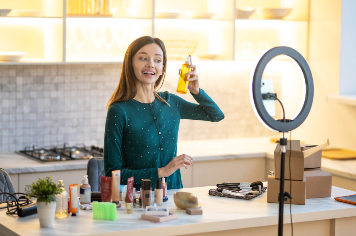 smiling young woman presenting hairspray during online beauty tutorial